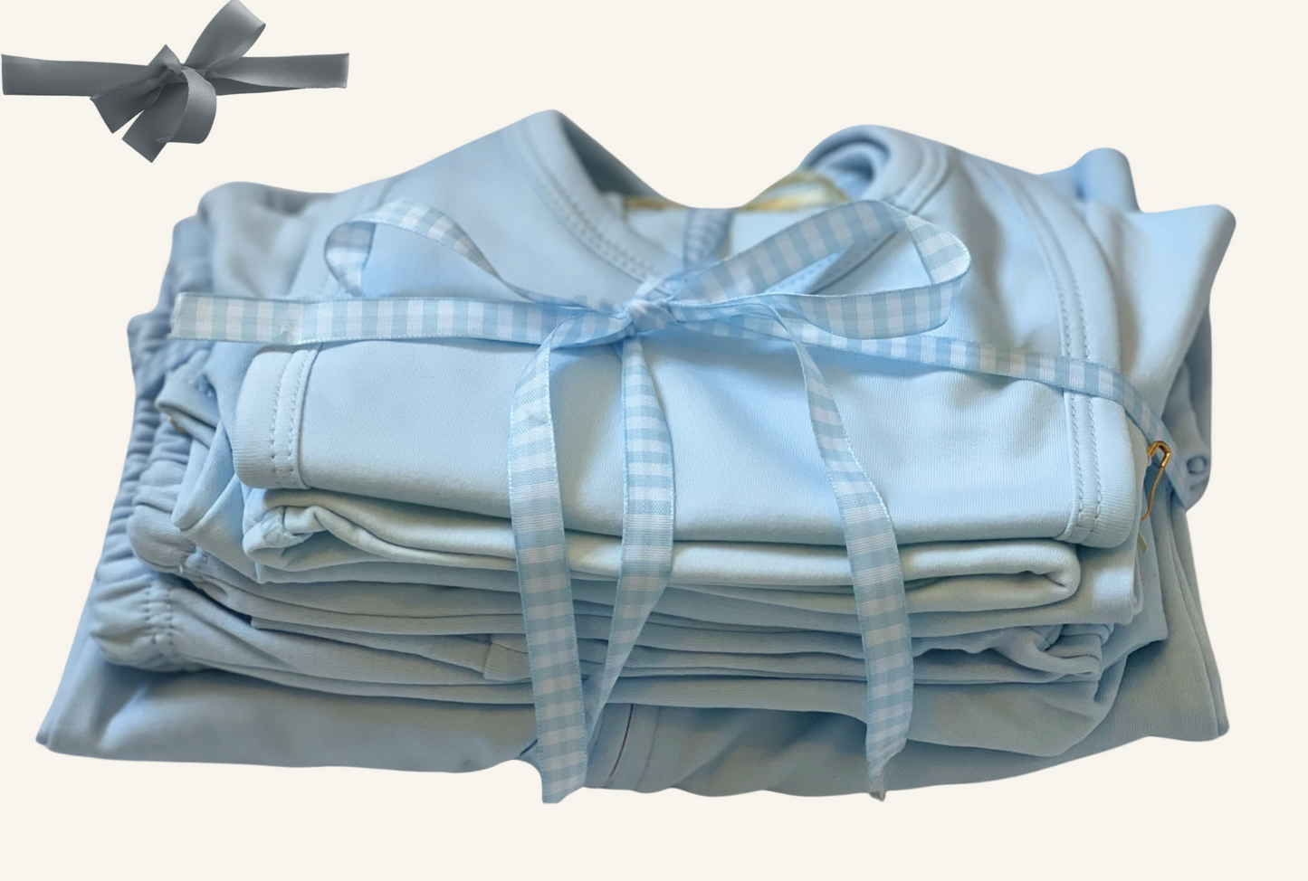 A stack of blue baby essentials including a sleep n play footie, pants, onesies, a hat, and a bib, all tied with a blue ribbon.